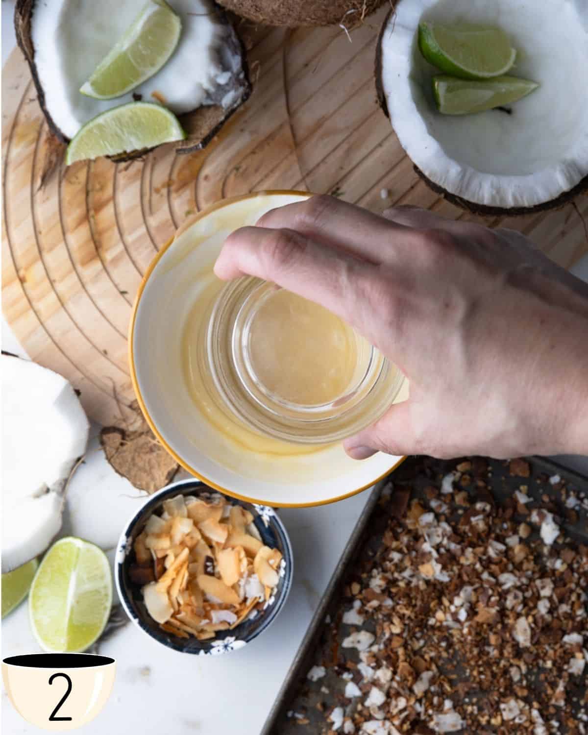 Hand dipping a glass rim into a shallow bowl of condensed coconut milk to rim the cocktail glass.