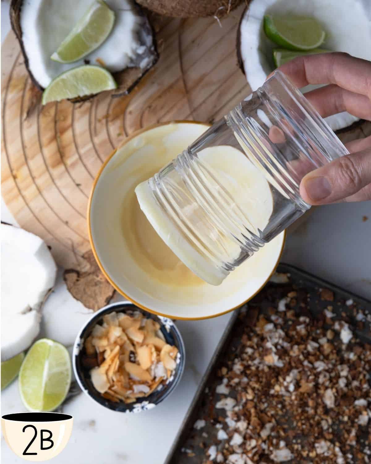 Hand pressing the rim of a glass into a plate of toasted coconut flakes.