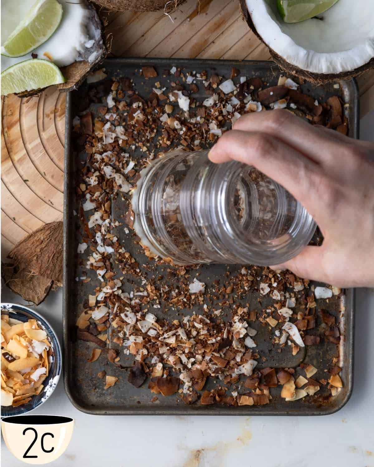 Hand pressing the rim of a glass into a plate of toasted coconut flakes.