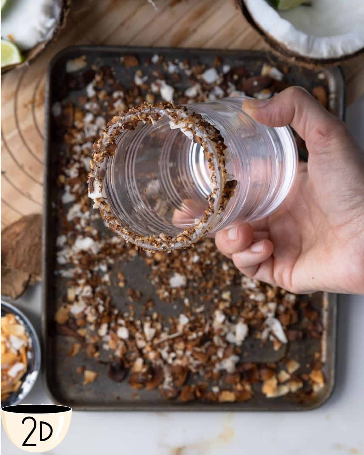 Glass with a rim coated in toasted coconut flakes on a baking tray.