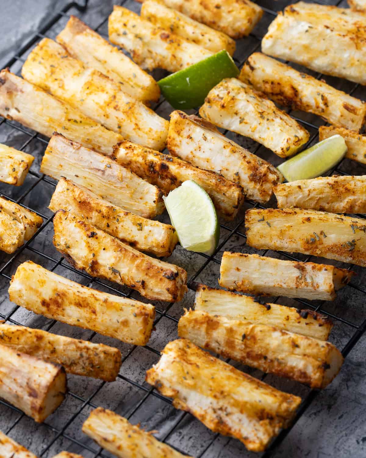 Close-up of crispy yuca fries garnished with fresh cilantro and sea salt, served with lime wedges.