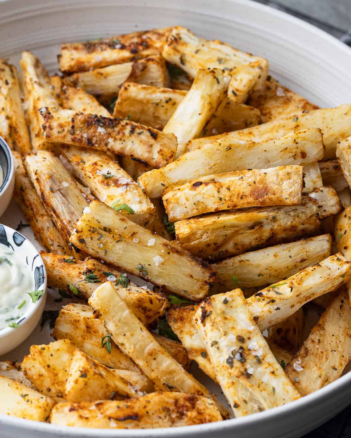 Close up image of crisy mandioca fries sitting in a bowl with dips and sprinkled with fresh cilantro.