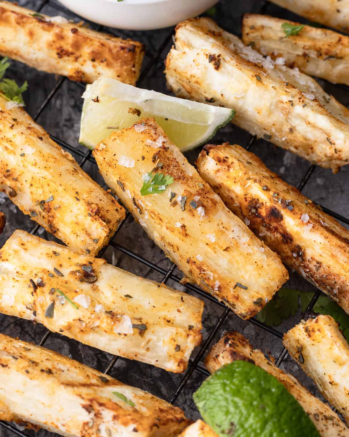 Seasoned yuca fries arranged on a wire rack, served with lime wedges and bowls of dipping sauces, garnished with cilantro.