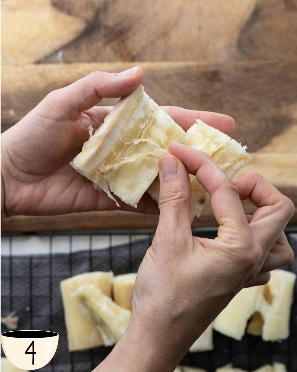 Two hands pulling apart a piece of boiled yuca to reveal and remove the fibrous core inside.