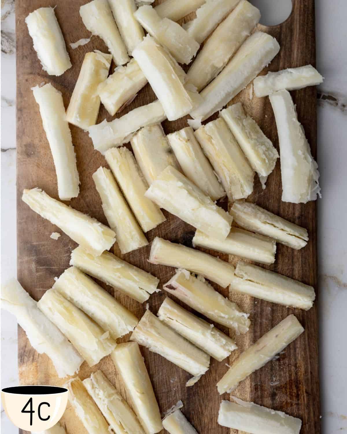 Boiled yuca pieces cut into fry-sized portions, spread out on a wooden cutting board.