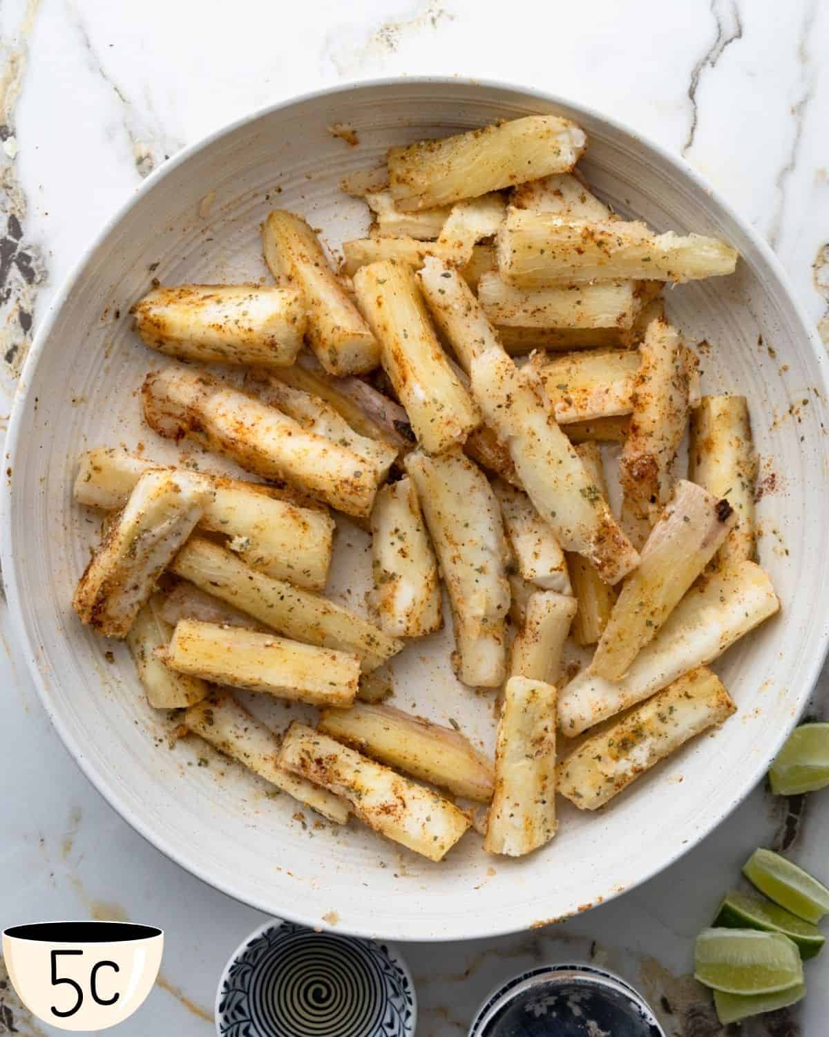 Seasoned yuca fries in a large white bowl, ready to be cooked, with lime wedges visible on the side.