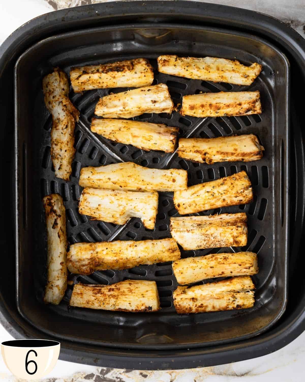 Seasoned yuca fries arranged in a single layer inside an air fryer basket, ready to be cooked.