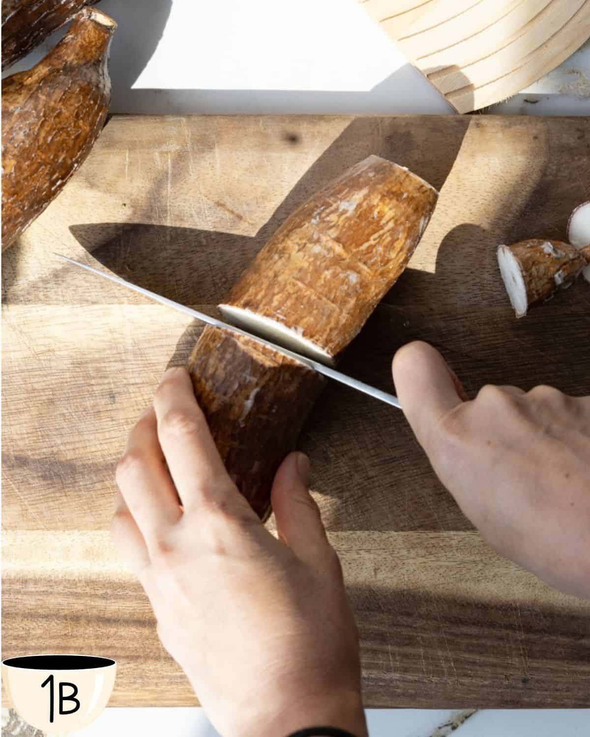 A hand slicing the yuca root into smaller, more manageable pieces on a wooden cutting board.