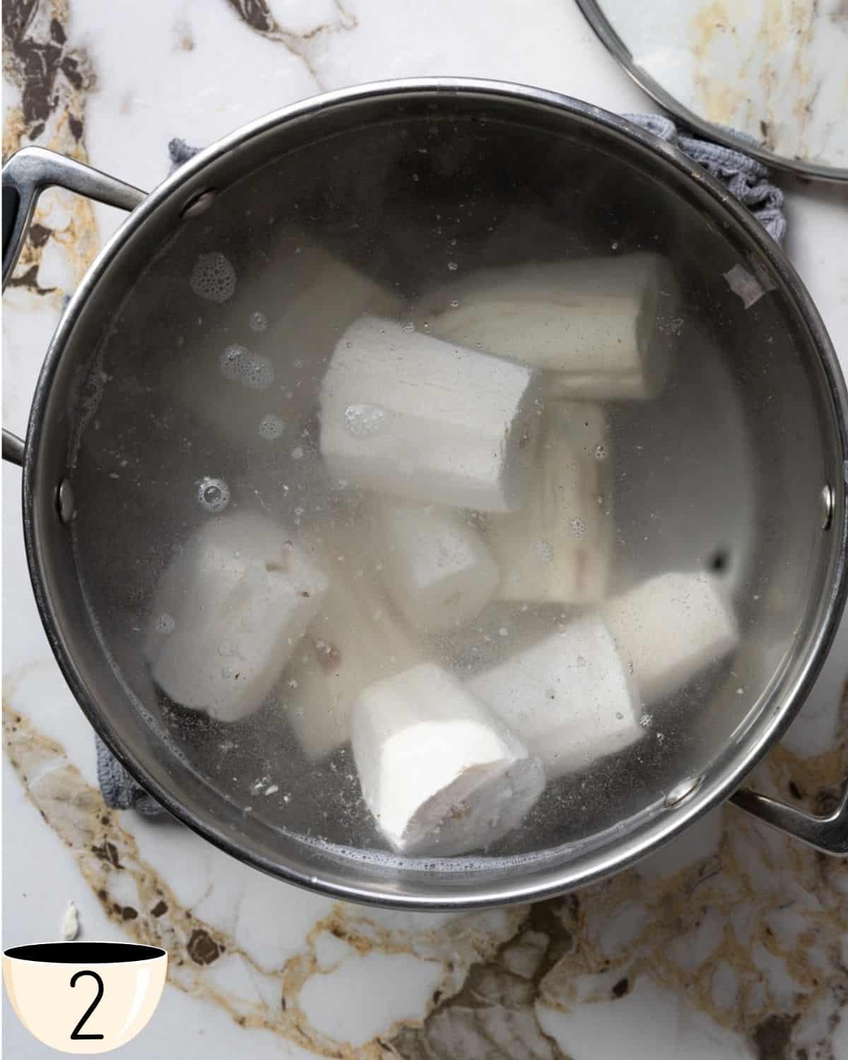 A pot of boiling water with yuca pieces submerged in it, cooking on the stove.