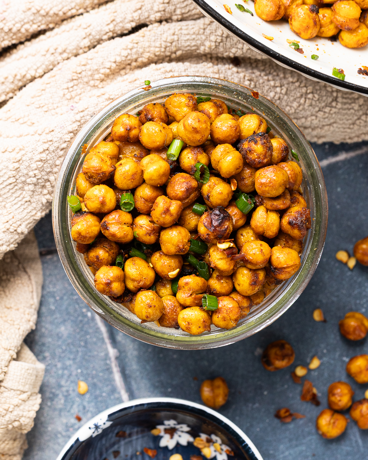 Top view of chickpeas in a glass jar with scattered chickpeas and green onion garnish.