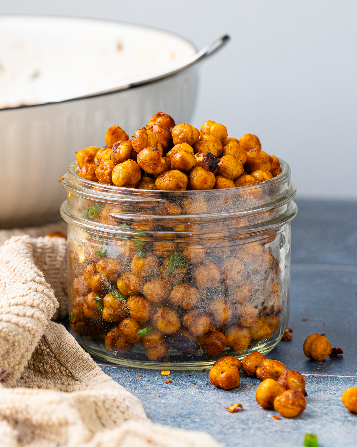 Side view of crispy chickpeas in a jar, with seasoning visible and chickpeas spilling out.