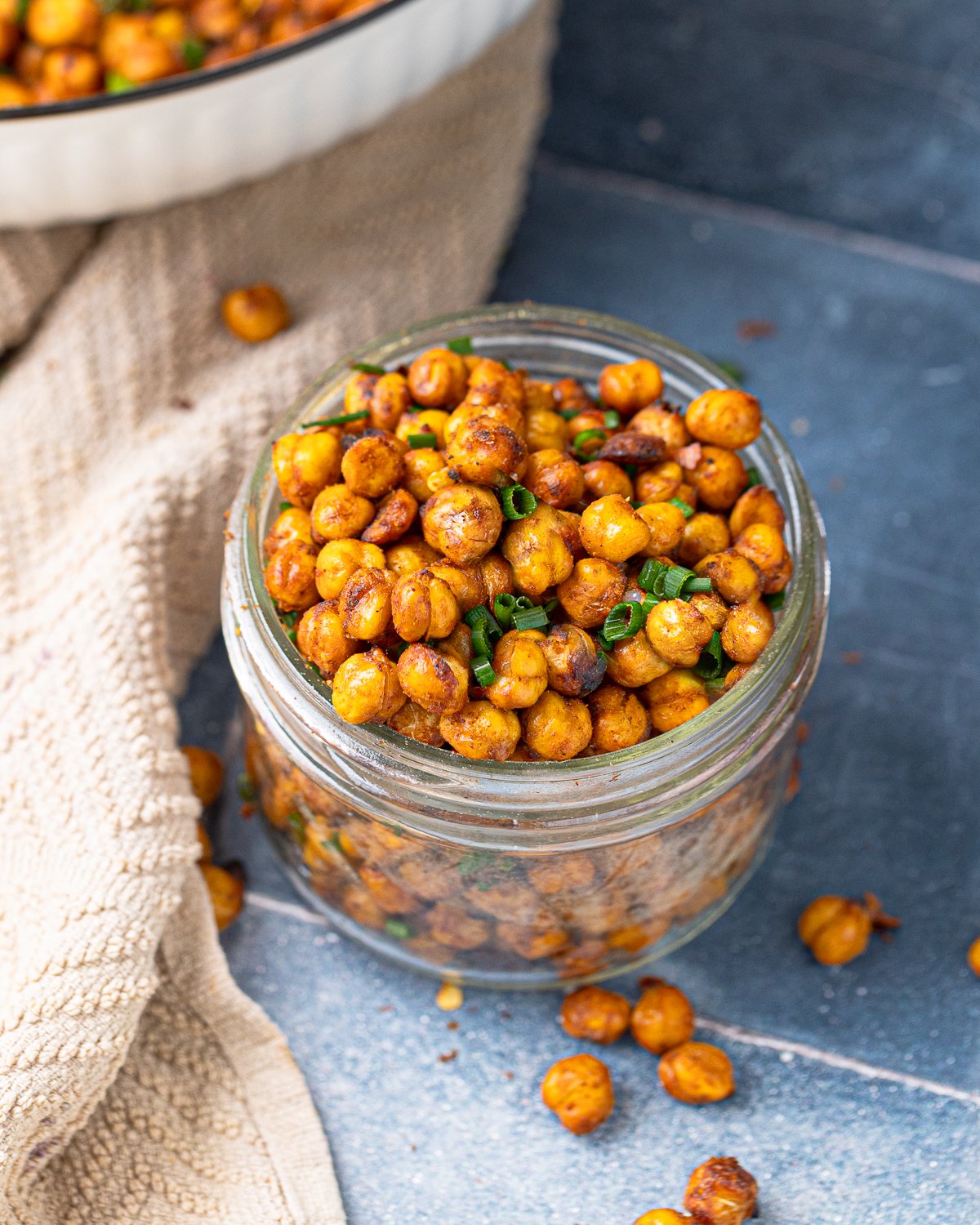 Crispy chickpeas in a glass jar, seasoned with chili, lime, and garnished with green onion.