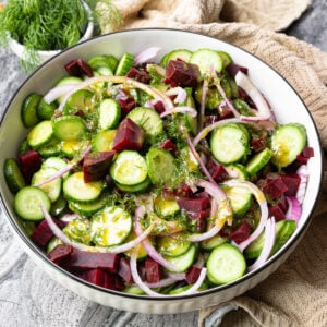 Cucumber beet salad in a serving bowl with red onion, fresh dill, and lemon-mustard dressing.