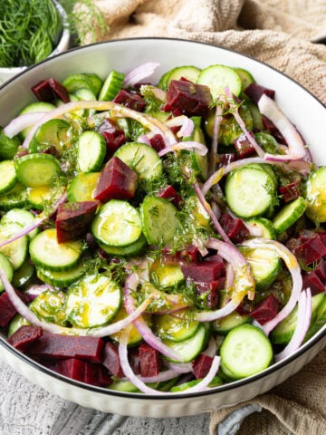 Cucumber beet salad in a serving bowl with red onion, fresh dill, and lemon-mustard dressing.